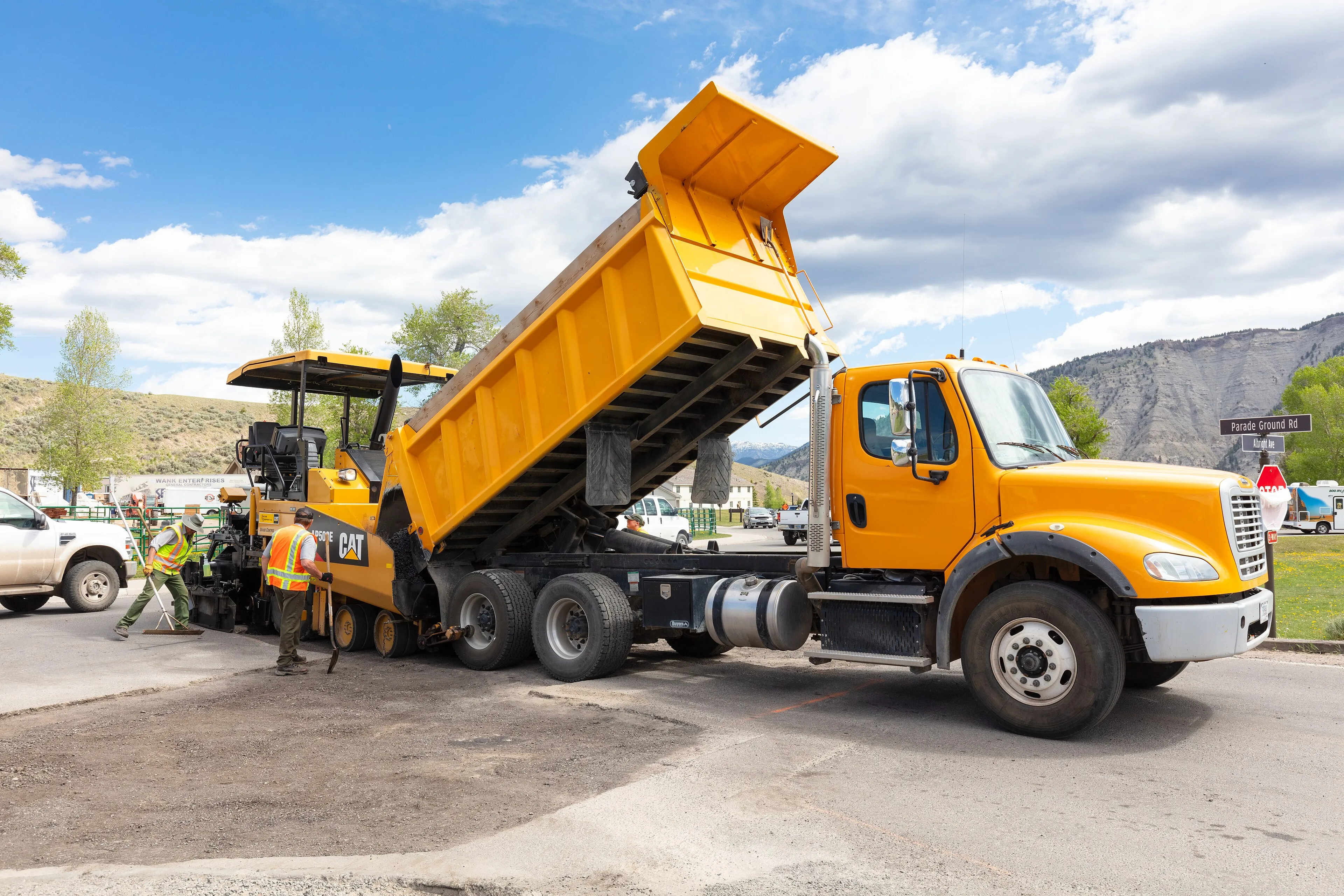 Crew paving a road with an orange asphalt truck